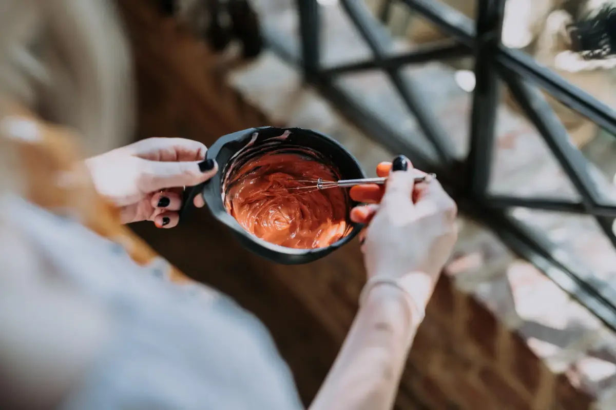 A George & Ivy colourist stirring a bowl of freshly mixed copper hair colour with a metal whisk, over the salon’s timber floor