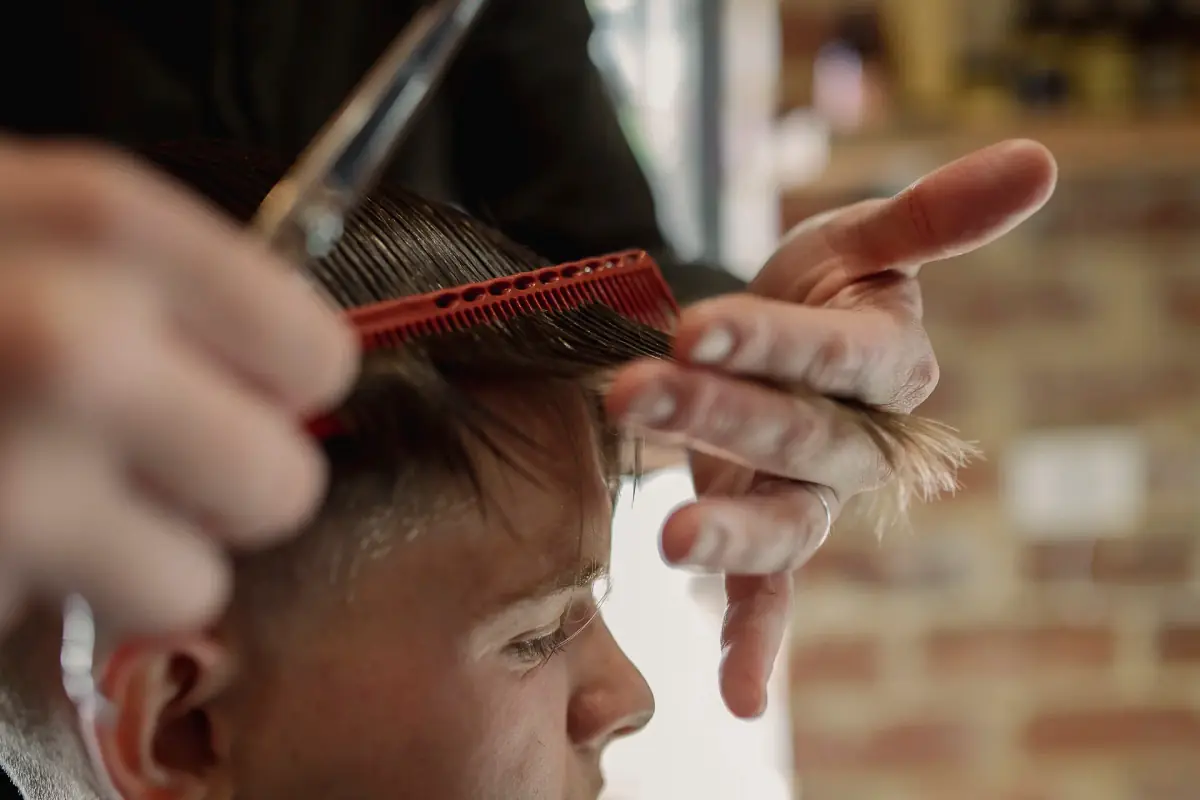 Close-up of a barber combing and scissor-cutting a man’s hair at George & Ivy, red brick wall behind