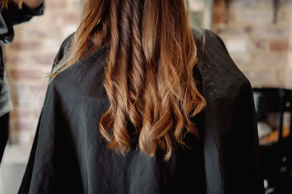 The back of a client in a black gown showing long copper hair extensions falling in loose waves past her shoulders