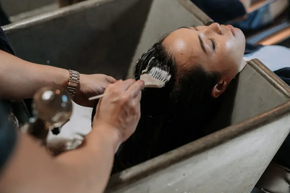 A stylist brushing a smoothing treatment through a reclining client’s long dark hair at the George & Ivy basin